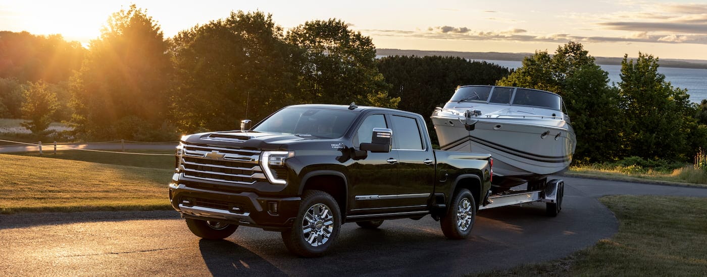 A black 2024 Chevy Silverado 2500 HD High Country is shown from the front at an angle while towing a boat after leaving a dealer that has a Chevy Silverado 2500 for sale.
