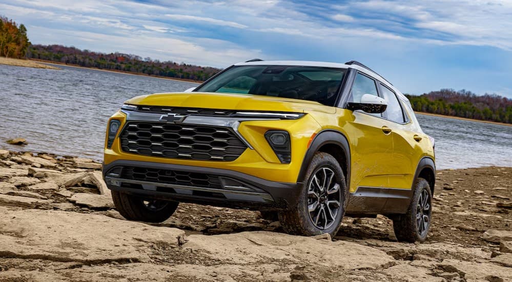 A yellow 2025 Chevy Trailblazer is shown parked off-road near a lake.