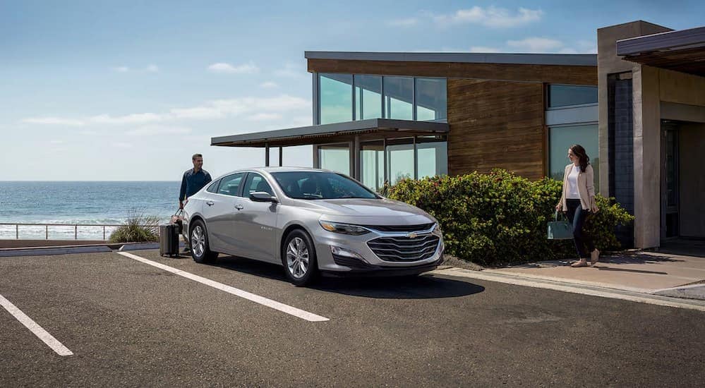 A silver 2025 Chevy Malibu is shown parked near an ocean.