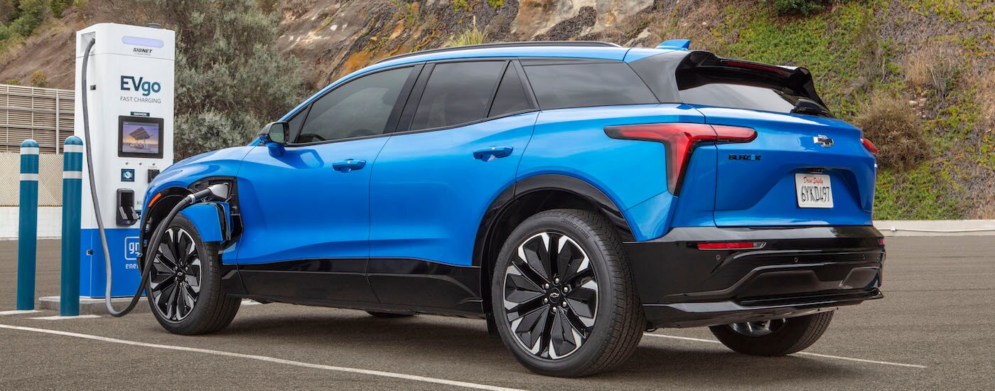 A blue 2024 Chevy Blazer EV for sale in Columbus is shown from the rear at an angle while charging.