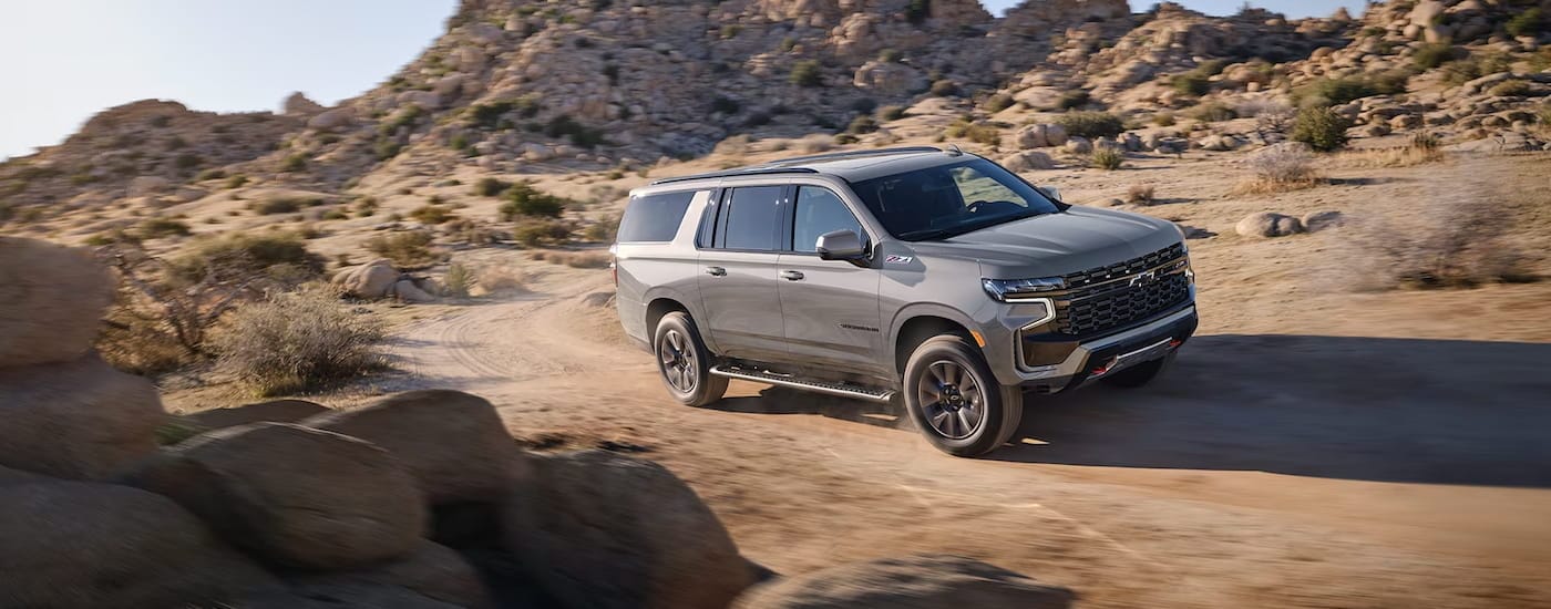 A grey 2024 Chevy Suburban Z71 is driving through a sandy area.