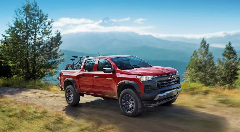 A red 2024 Chevy Colorado Trail Boss is shown driving off-road after visiting a Chevy dealer near Albany.