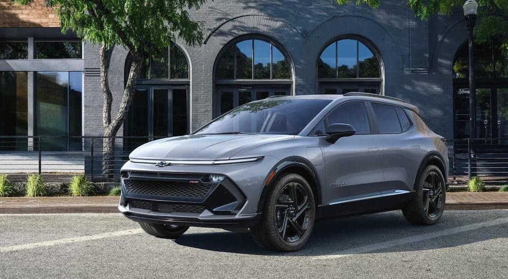 A silver 2025 Chevy Equinox EV RS is shown parked near a brick building.