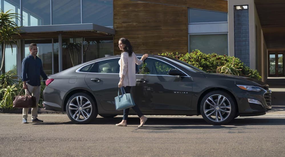 A gray 2025 Chevy Malibu is shown parked near two people.