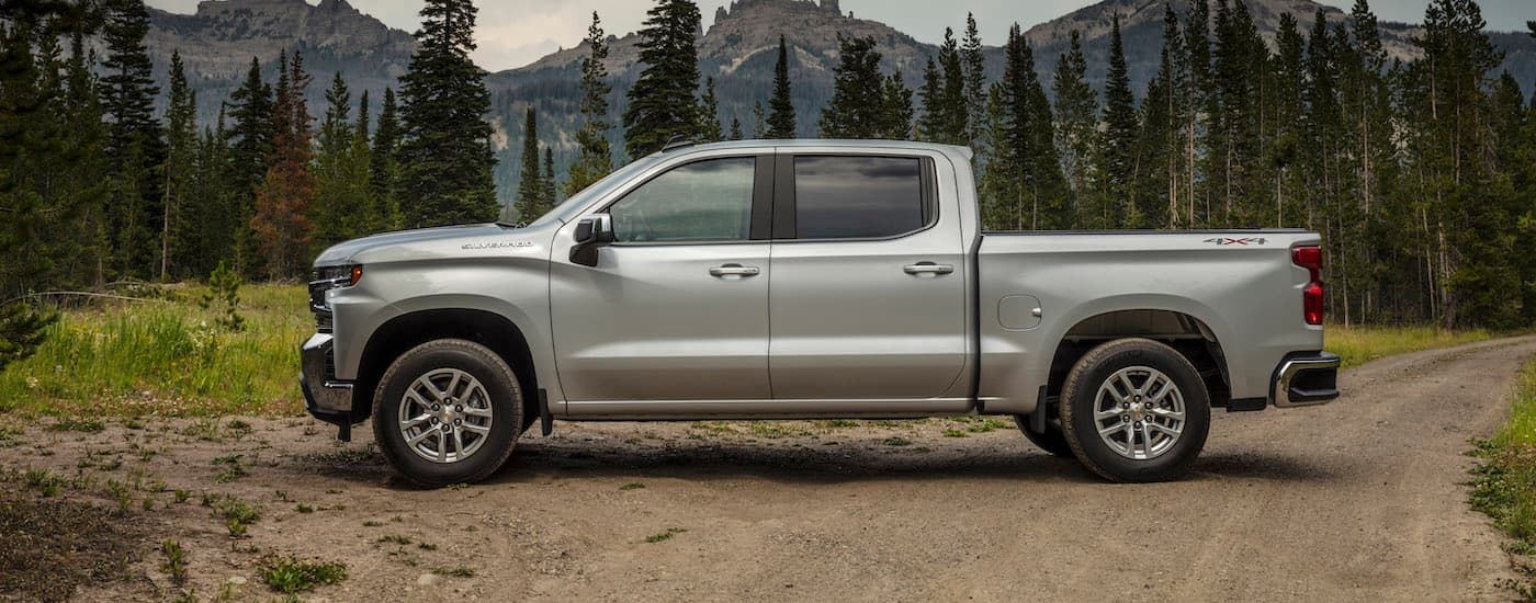 A silver 2020 Chevy Silverado 1500 LT is shown from the side on a dirt trail after visiting a Chevy dealer near you.