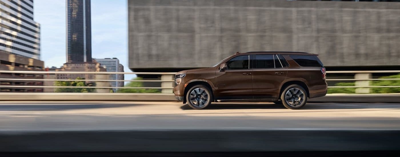 A brown 2022 Chevy Tahoe is shown from the side driving on a city street in Columbus, OH after looking at Chevy SUVs for sale.
