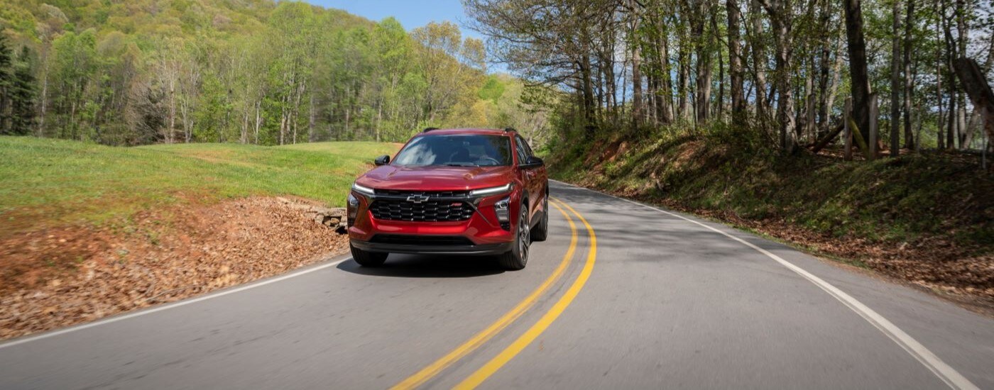 A red 2024 Chevy Trax RS is shown driving on a tree-lined road.