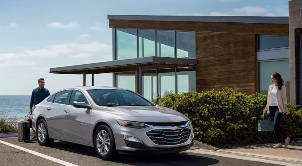 A silver 2024 Chevy Malibu is shown parked near a house.