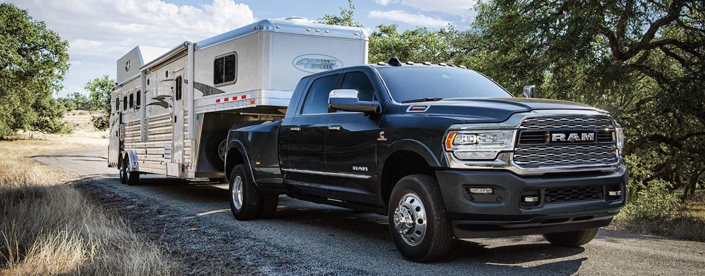 A black 2019 Ram 3500 is shown towing a long white trailer after leaving a used truck dealer.