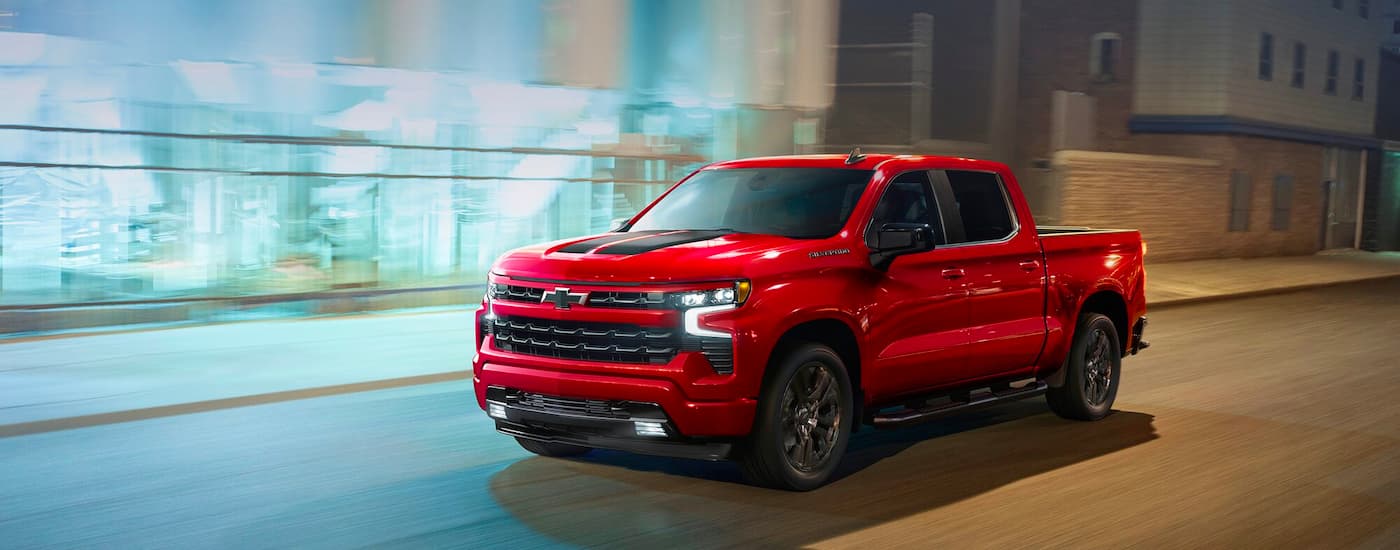One of the most popular Chevy trucks for sale, a red 2023 Chevy Silverado 1500 RST, is shown driving on a city street.