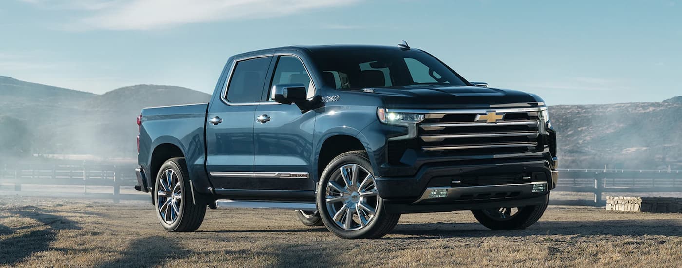 A blue 2022 Chevy Silverado 1500 High Country is shown parked on a farm.