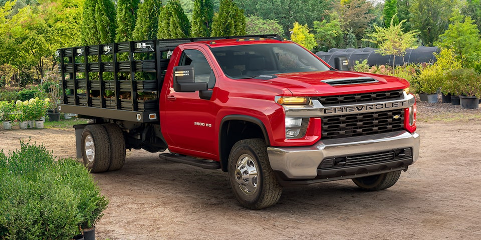 A red 2022 Chevy Silverado 3500 Chassis Cab is shown with a bed full of trees.