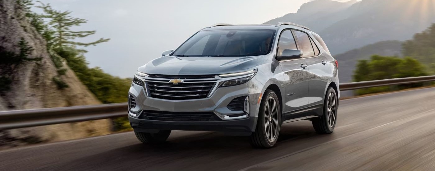A grey 2023 Chevy Equinox for sale is shown driving on a mountain road.