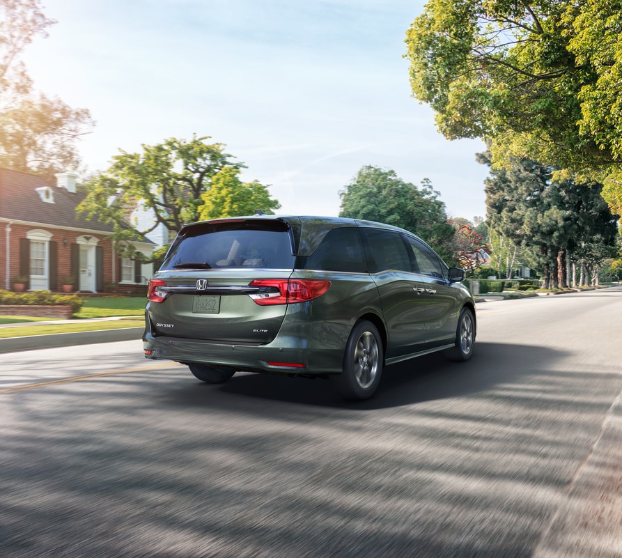 dark green Honda Odyssey minivan driving through a suburban neighborhood