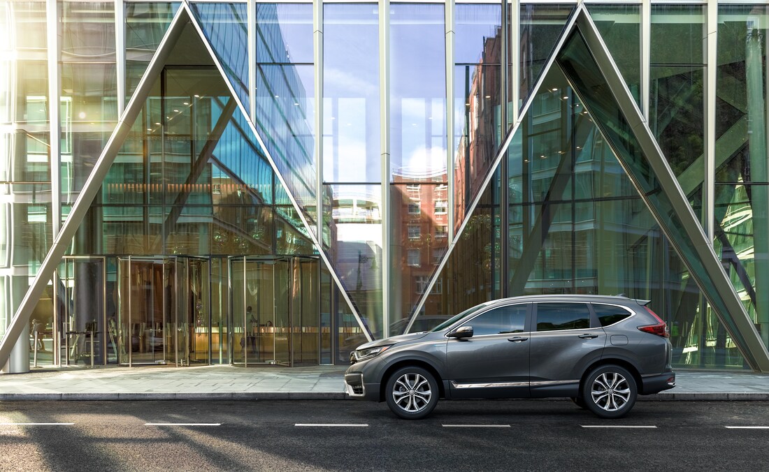 silver Honda CR-V hybrid SUV parked in front of a modern building with triangular windows