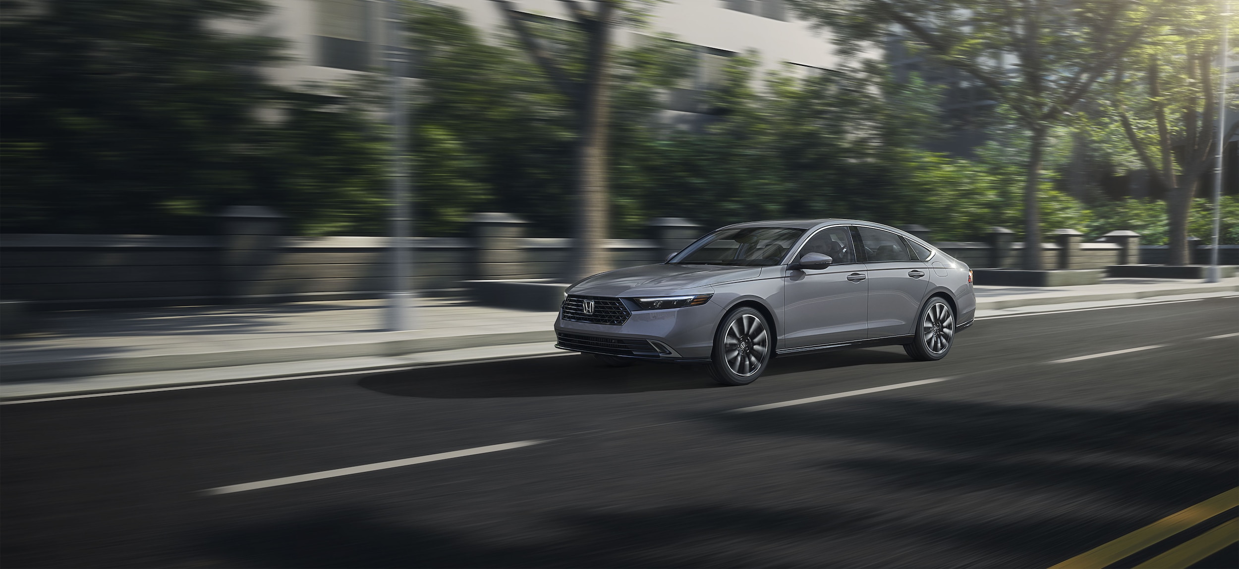 grey Honda Accord hybrid driving on a tree-lined downtown street