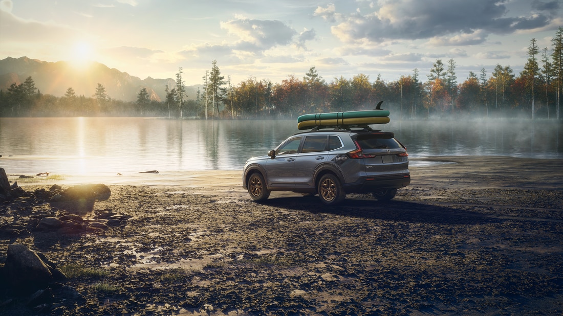silver Honda CR-V SUV parked at a lake beach at sunset with paddleboards on the roof rack