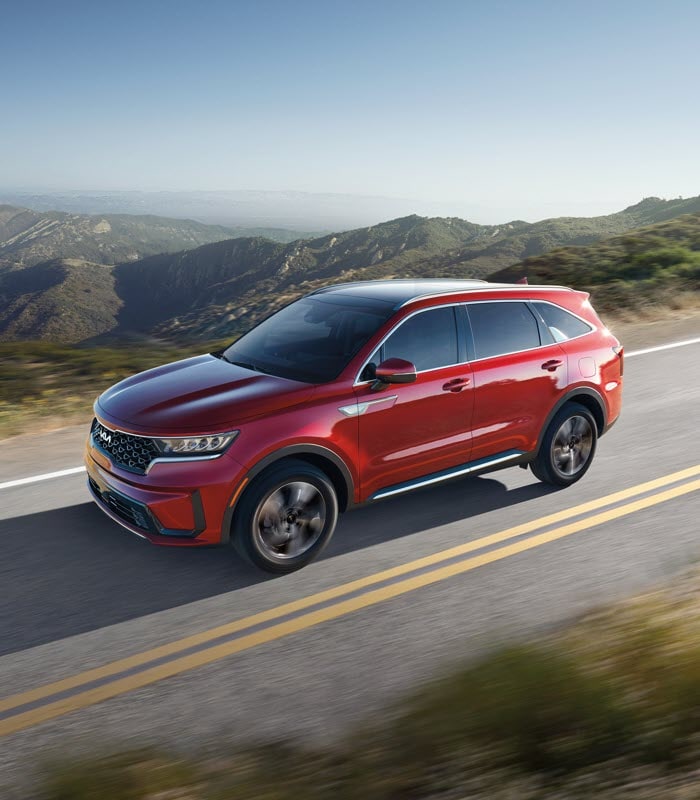 2021-KIA-Sorento-SXPrestige-XLinePackageSUV.png green Kia Sorento SUV driving through the mountains with blue skys