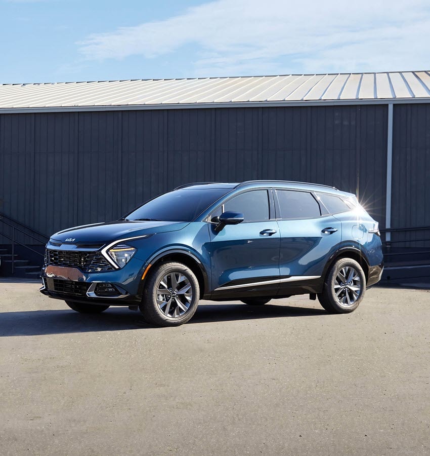 2021-KIA-Sportage-SX-SUV-L03.png white Kia Sportage SUV parked on a white-rocked ledge with a blue sky in the background