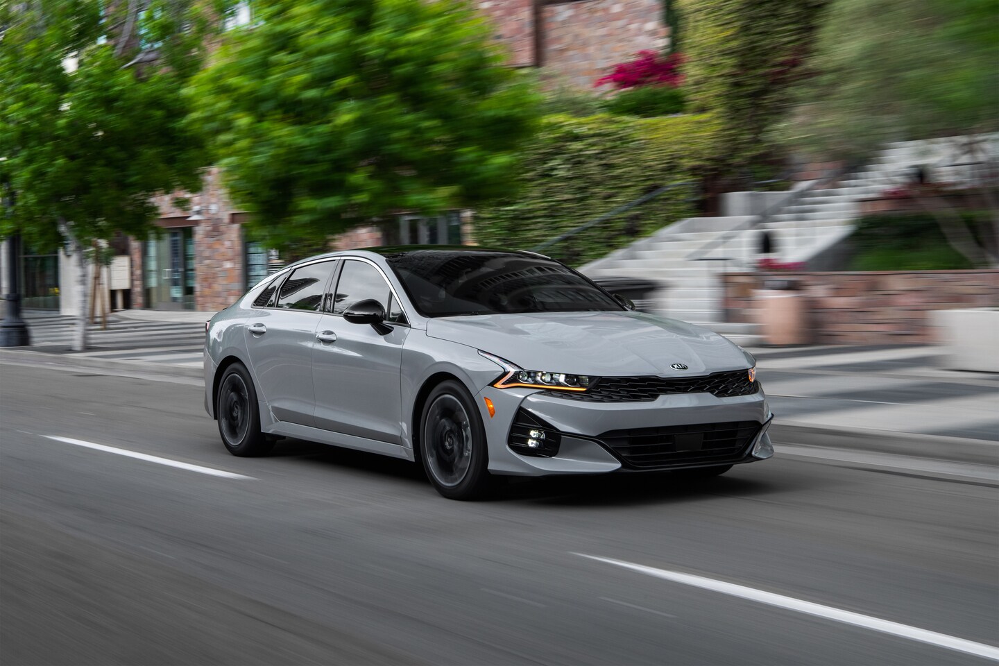 grey Kia K5 driving through a town