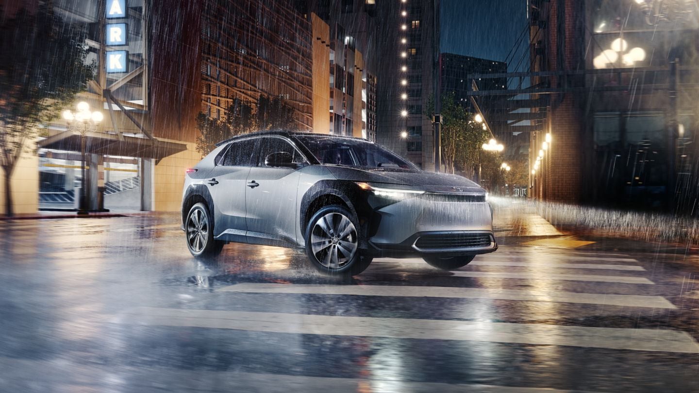 silver Toyota BZ4X driving through a city in the rain