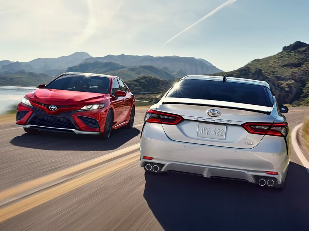 red and white Toyota Camry hybrids driving past each other on a curved road