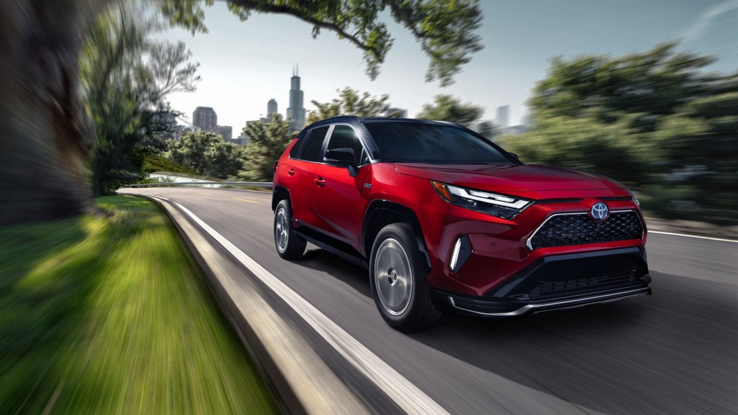 red Toyota RAV4 Prime driving fast on a road lined with greenery
