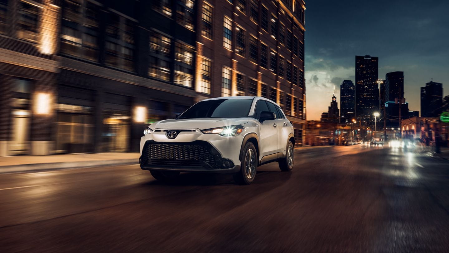 white Toyota Corolla Cross driving down a city street at night