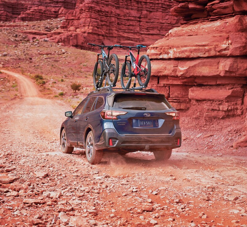 blue Subaru Outback SUV driving on a red desert road with bikes on the roof rack