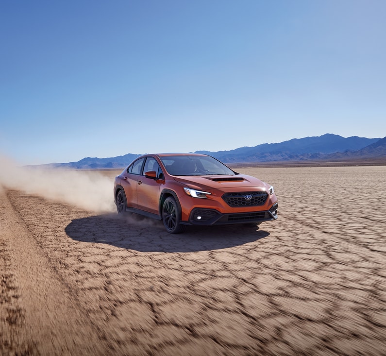 orange Subaru WRX sports sedan driving fast along a cracked desert