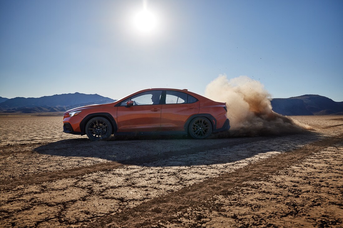 orange Subaru WRX sedan kicking up dust on a cracked desert