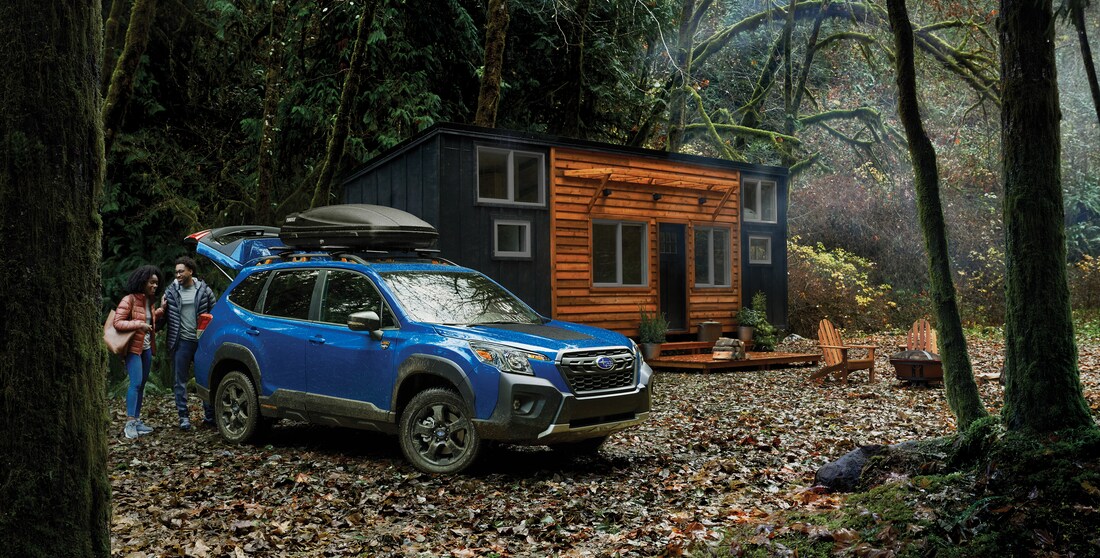 blue Subaru Forester SUV parked in front of a small cabin