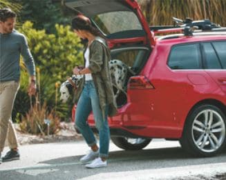 A couple getting their dalmatian out of a Volkswagen hatchback trunk