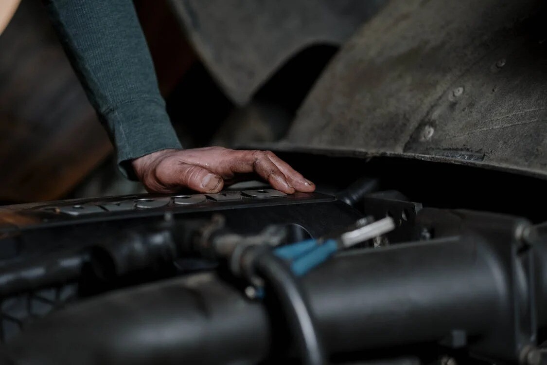 The hand of a mechanic working under the hood of a unknown vehicle
