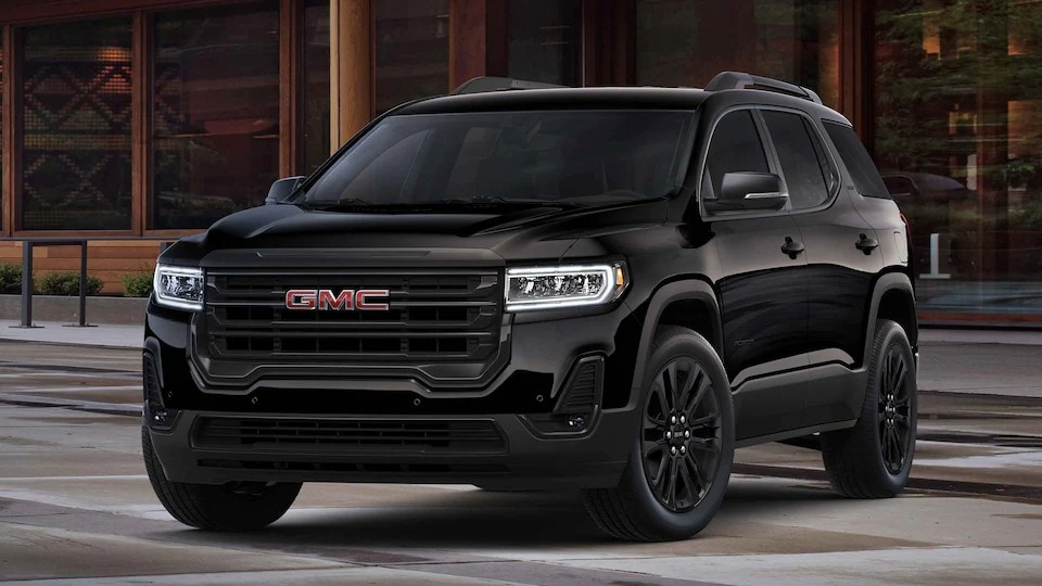 Black 2023 GMC Acadia parked in the street in front of a wooden city building