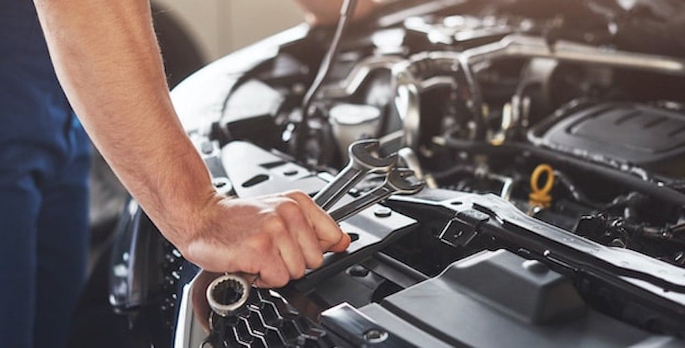 Technician Holding Wrenches Working on Engine