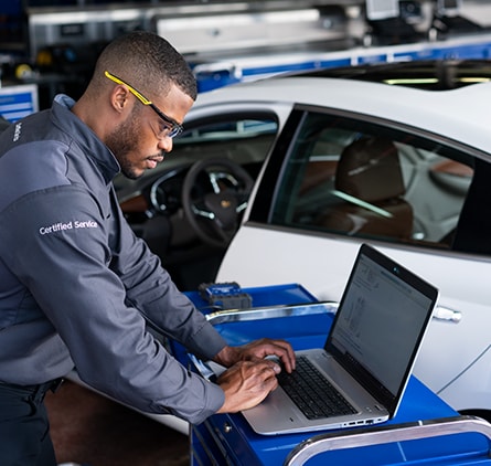 service technician typing on laptop in dealership service shop