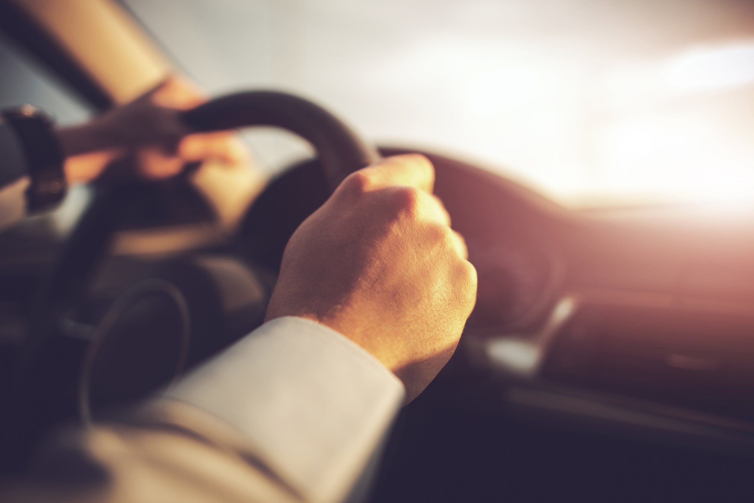 Driver's hands on a steering wheel in warm sunlight, Dennis & Co. Auto Group