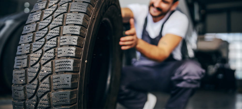 Smiling technician beside a tire at a Dennis & Co. Auto Group service center