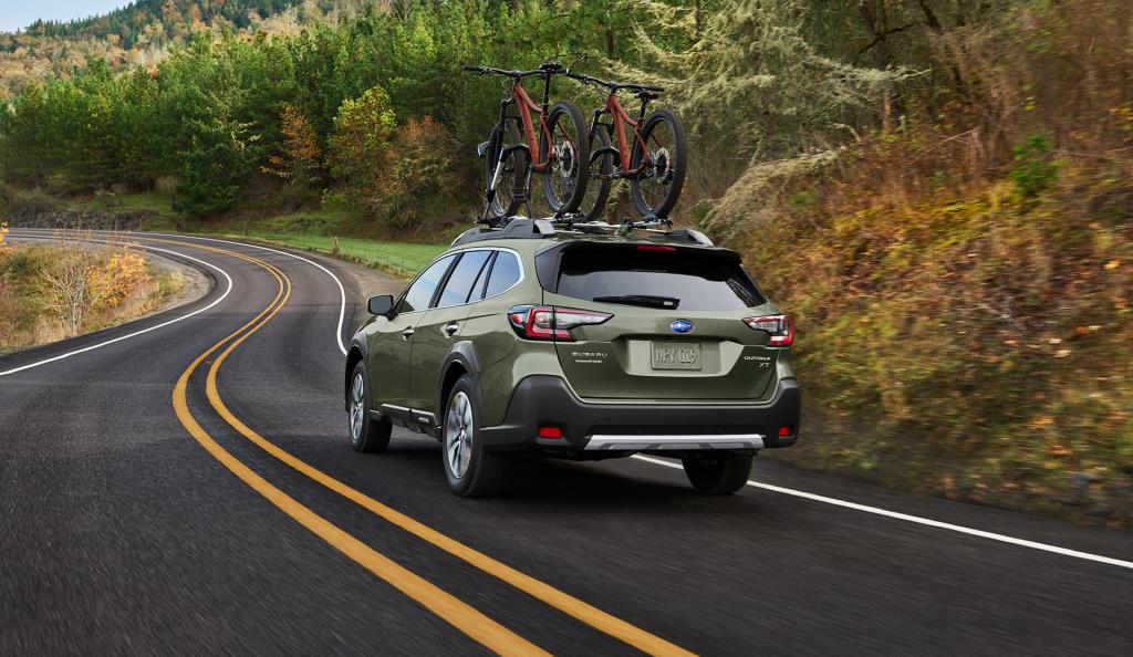 vue latérale arrière d'une Subaru Outback 2023 transportant des vélos sur une route en forêt