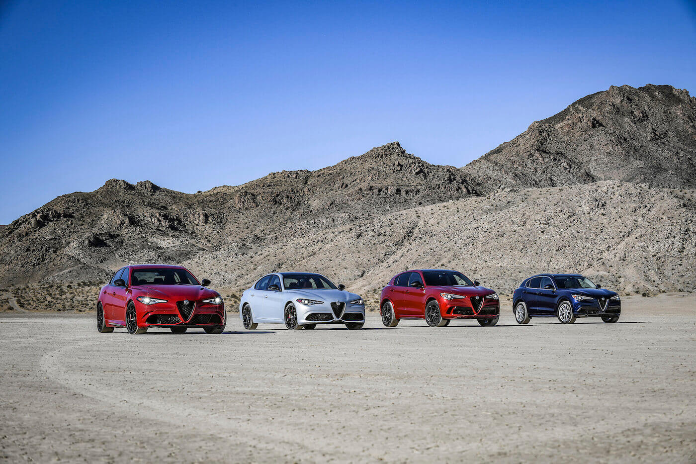 Quatre véhicules Alfa Romeo 2020 incluant deux Giulia et deux Stelvio garés côtes-à-côtes dans un désert