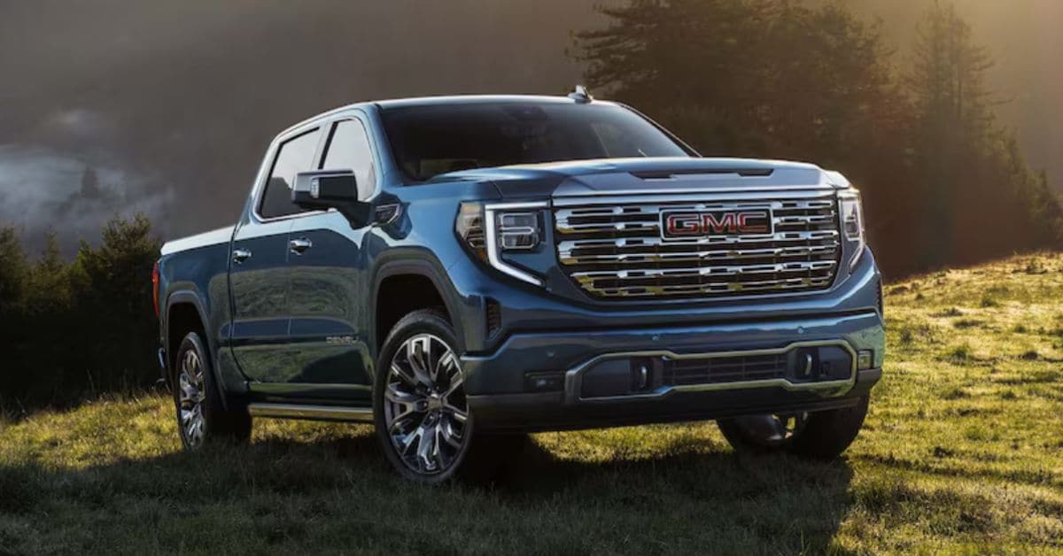 Blue GMC Sierra 1500 parked on grass in front of a forest