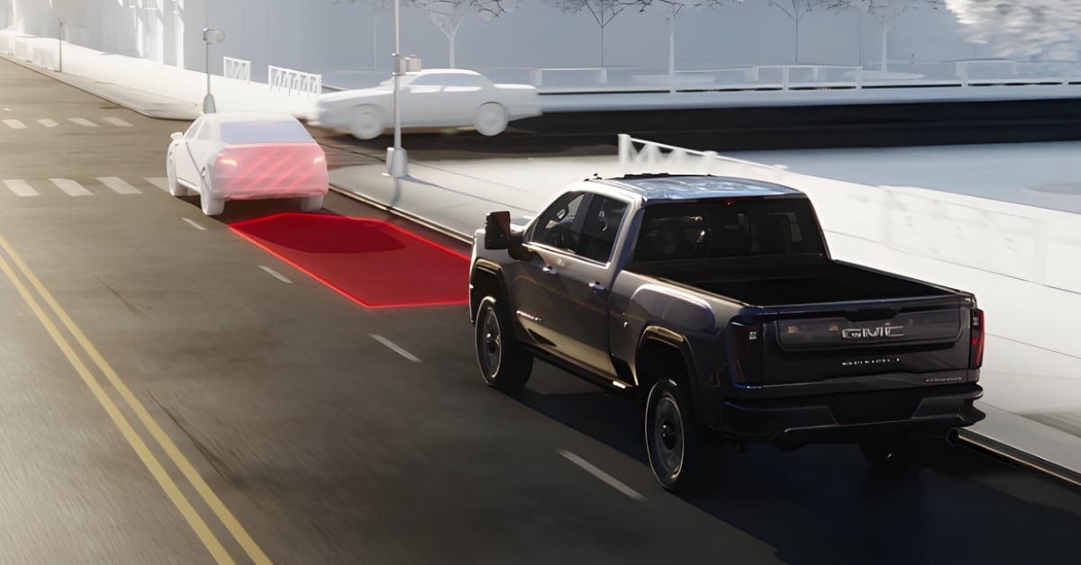  A digital rendering of a dark-colored 2026 GMC Sierra 2500 HD Denali pickup truck driving in an urban environment. The truck is shown from a rear three-quarter perspective, featuring chrome 