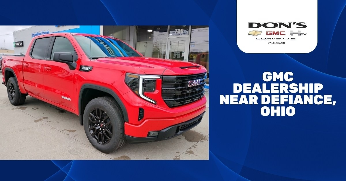  A bright red GMC Sierra pickup truck parked in front of a dealership building with signs reading 