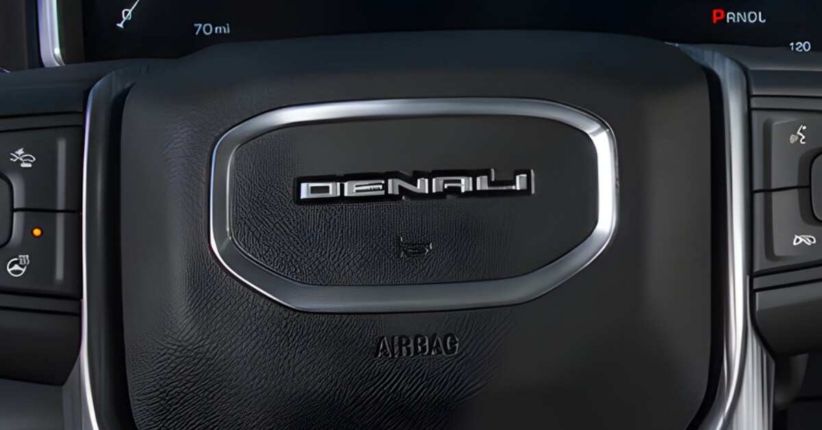  A close-up view of a 2026 GMC Sierra 2500 HD Denali steering wheel featuring textured black material, chrome accents, and the 
