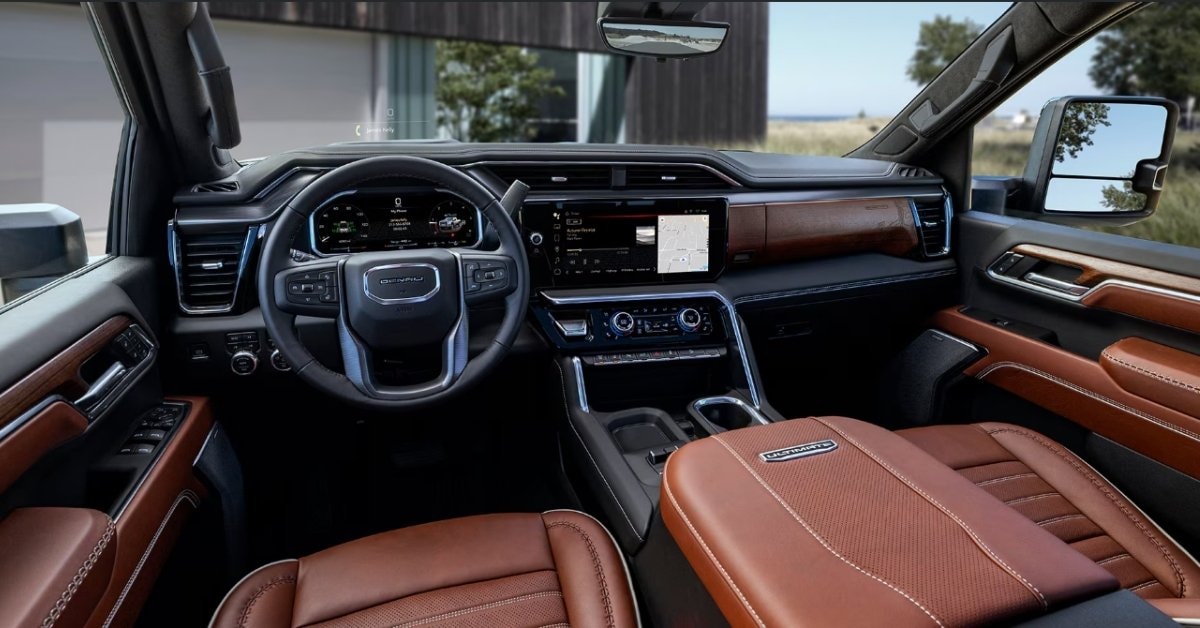  The luxurious interior of a 2026 GMC Sierra 2500 HD Denali Ultimate pickup truck, featuring Alpine Umber leather seats with white contrast stitching, a leather-wrapped steering wheel with the 