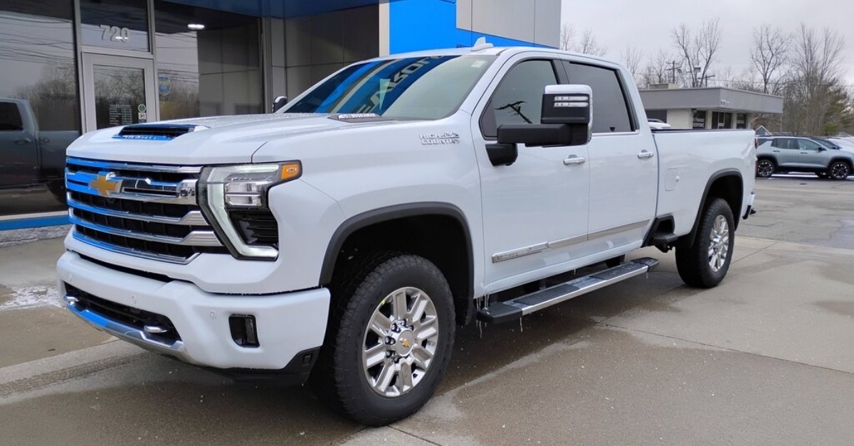  A white 2026 Chevrolet Silverado 2500 HD High Country pickup truck is parked at Don's Chevrolet GMC, angled slightly to the left. The truck features a large chrome grille with blue accents, 