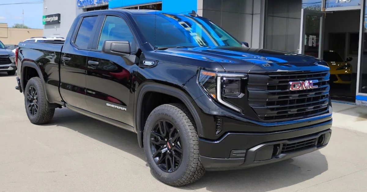  A sleek 2026 black GMC Sierra 1500 pickup truck parked on a paved lot outside Don's Chevrolet GMC. The truck features a bold grille with the red GMC logo, C-shaped LED headlights, and black wheels with all-terrain tires. The background includes a building with a 'Certified Service' sign, a green 'Enterprise' sign, and a yellow sports car visible through the dealership's glass windows.