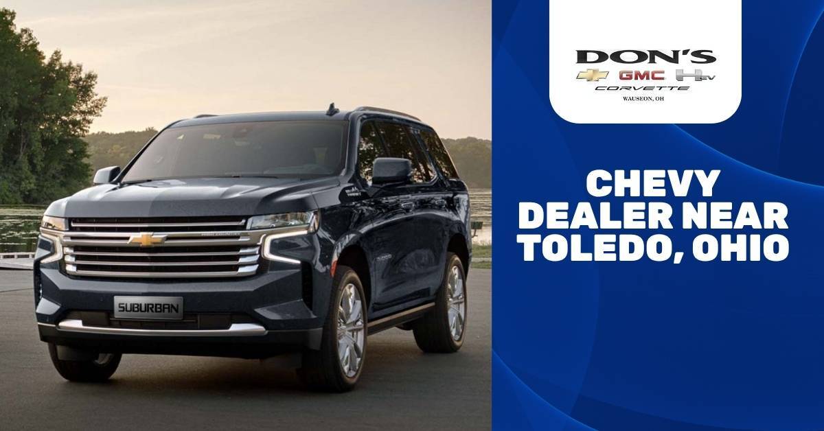  A dark gray Chevrolet Suburban High Country SUV is parked on an asphalt surface near a scenic waterfront during golden hour, with a backdrop of trees and a hazy sky. The right side of the image features a dark blue background with bold white text reading 