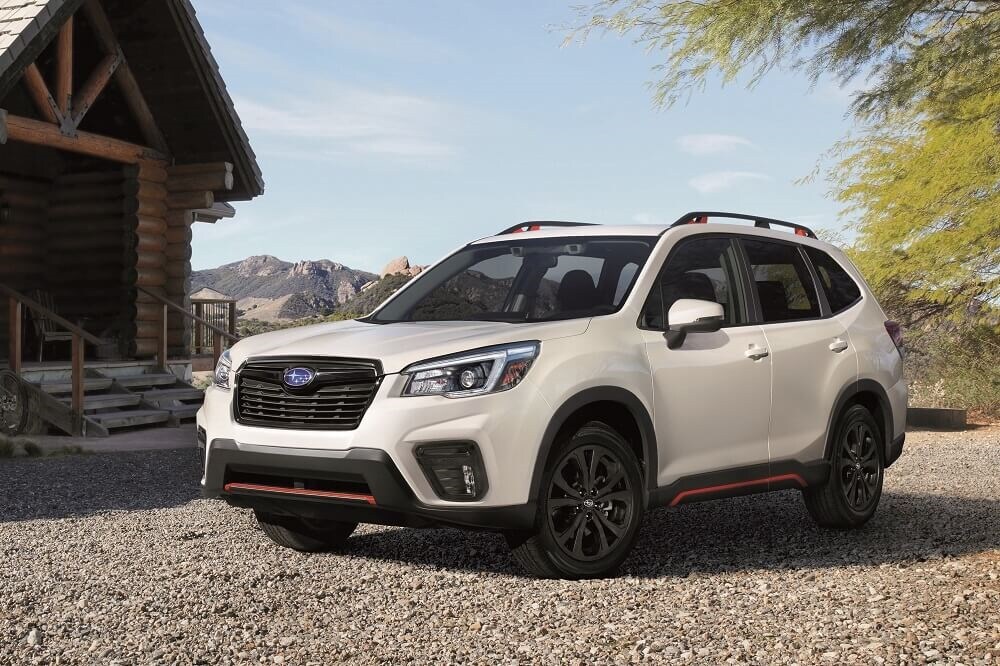 white Subaru Forester SUV parked in front of a log cabin